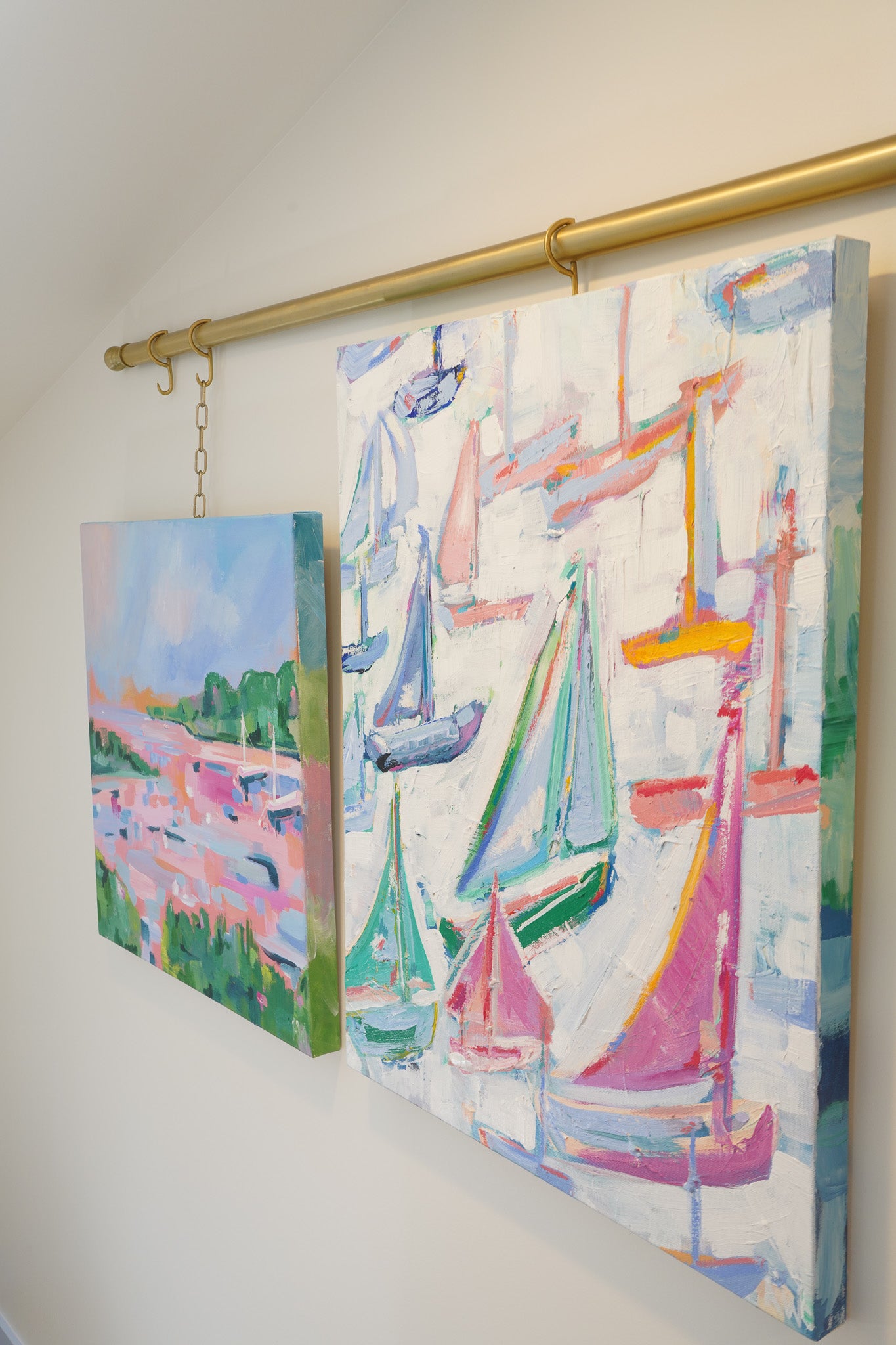 2 paintings shown hung side by side. One a landscape, depicting two sailboats at moorings in a bay. The other an abstract painting depicting many very colorful sailboats. Both inspired by northern Michigan and both full of pinks, greens, blues and oranges. Painted by artist Alexandra Williams 